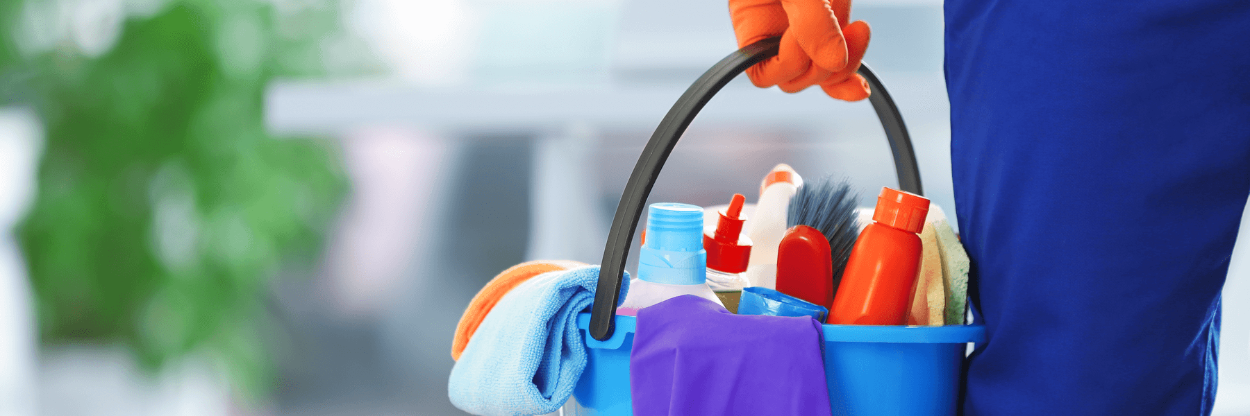 Man wearing glove carrying bucket full of different cleaning products and supplies